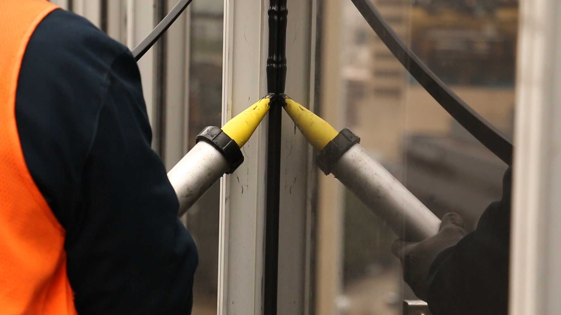 Workers applying Spectrem 1 black silicone sealant to a vertical window mullion using dual caulking guns