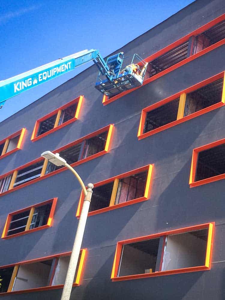 Workers installing Cat 5 rain screen barrier on college building facade