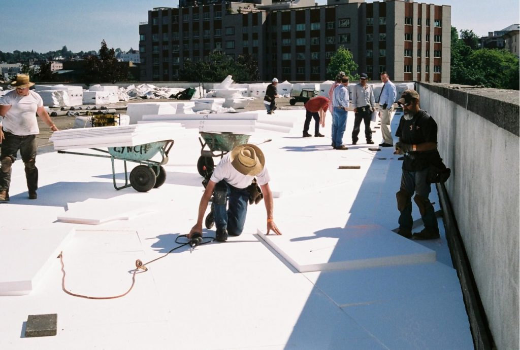 Contractors installing EPS insulation on a flat commercial roof for energy efficiency