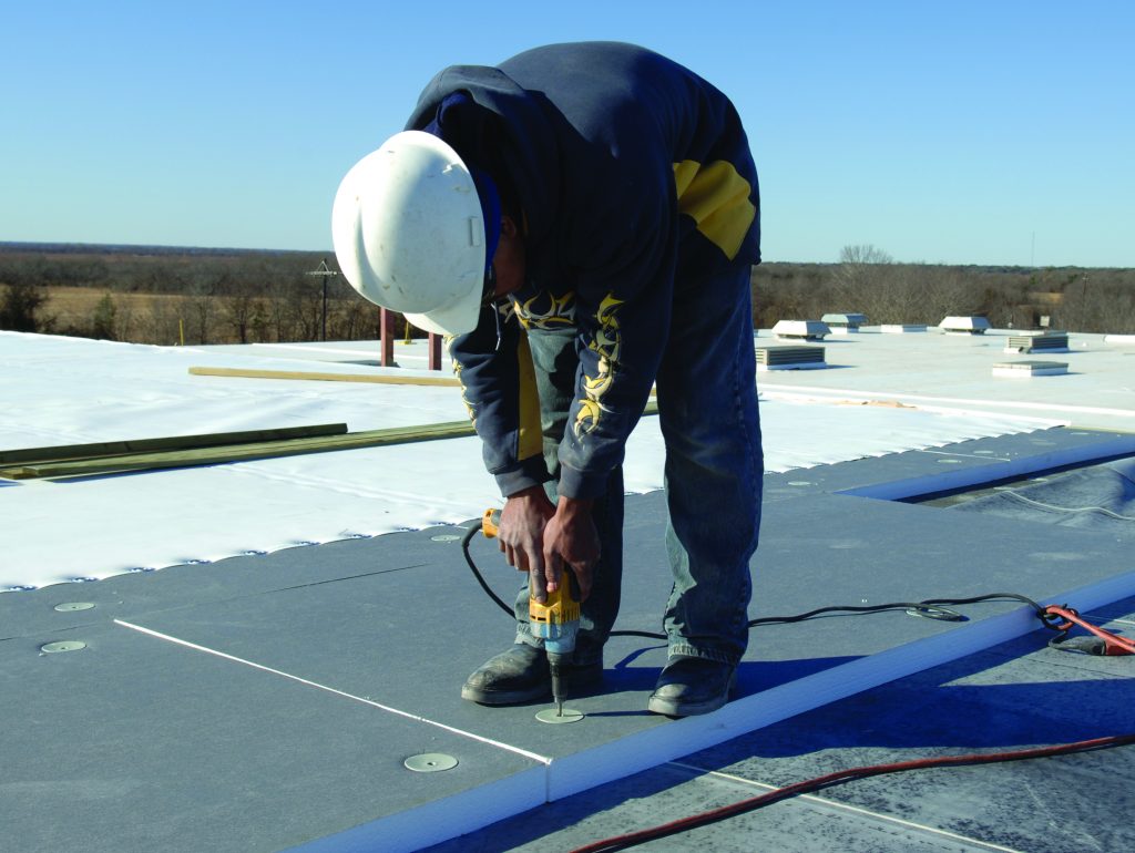 Worker fastening rigid foam insulation on a commercial flat roof installation