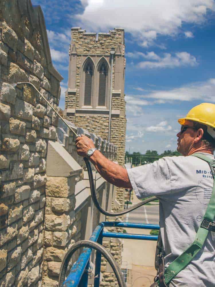 Worker applying Siloxane PD water repellent to stone masonry